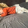 child, toddler, sleeping, bed, pajamas, orange_clothing, curly_hair, pillow, blanket, indoors, rest, peaceful, cozy, person, soft_lighting, relaxation, home, sleep, young_child, casual