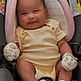 baby, infant, child, smiling, car_seat, onesie, striped_clothing, mittens, socks, floral_pattern, headrest, buckle, seat_padding, rosy_cheeks, portrait, closeup, hands, legs, warning_label, pink