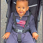 Ayden a rejoint le concours — aidez-le/la à gagner de superbes lots ! american_flag, baby, casual, child, clothing, daylight, face, footwear, hands, happy, head, jogging_pants, outdoor, pavement, person, portrait, seatbelt, stroller, sweater, toddler