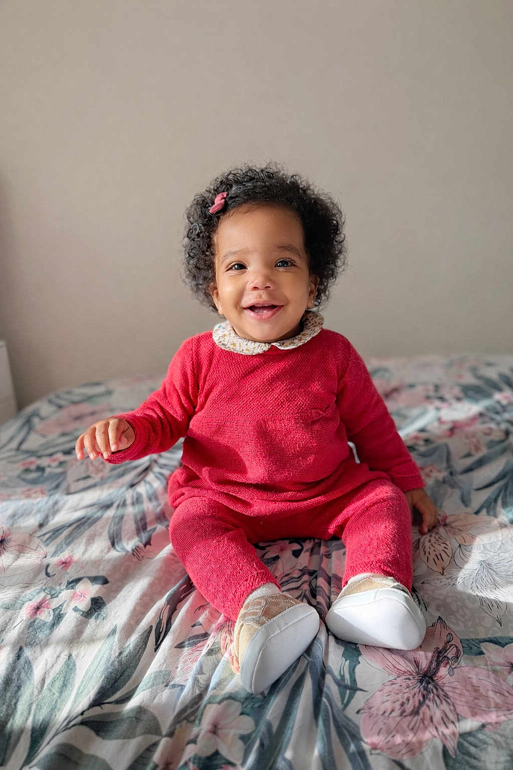 Jaïa participe au concours pour gagner de l'argent avec cette photo : baby, toddler, child, smiling, curly_hair, hair_bow, red_outfit, onesie, sitting, bed, bedding, floral_pattern, white_shoes, portrait, indoor, happy, cute, skin, eyes, hands