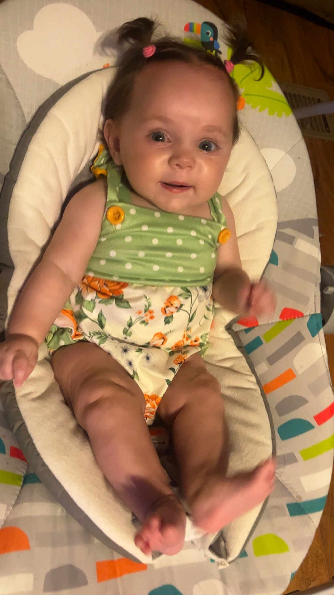 Remington is registered to the contest to win money with this photo: baby, infant, child, pigtails, green_clothing, floral_pattern, baby_seat, blanket, cushion, smile, face, legs, feet, wooden_floor, indoor, cute, happy, person, portrait, toddler