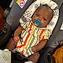 baby, infant, pacifier, car_seat, striped_clothing, footwear, white_shoes, child, indoors, seatbelt, headrest, patterned_fabric, baby_gear, wooden_floor, cute, portrait, person, small_child, sitting, clothing
