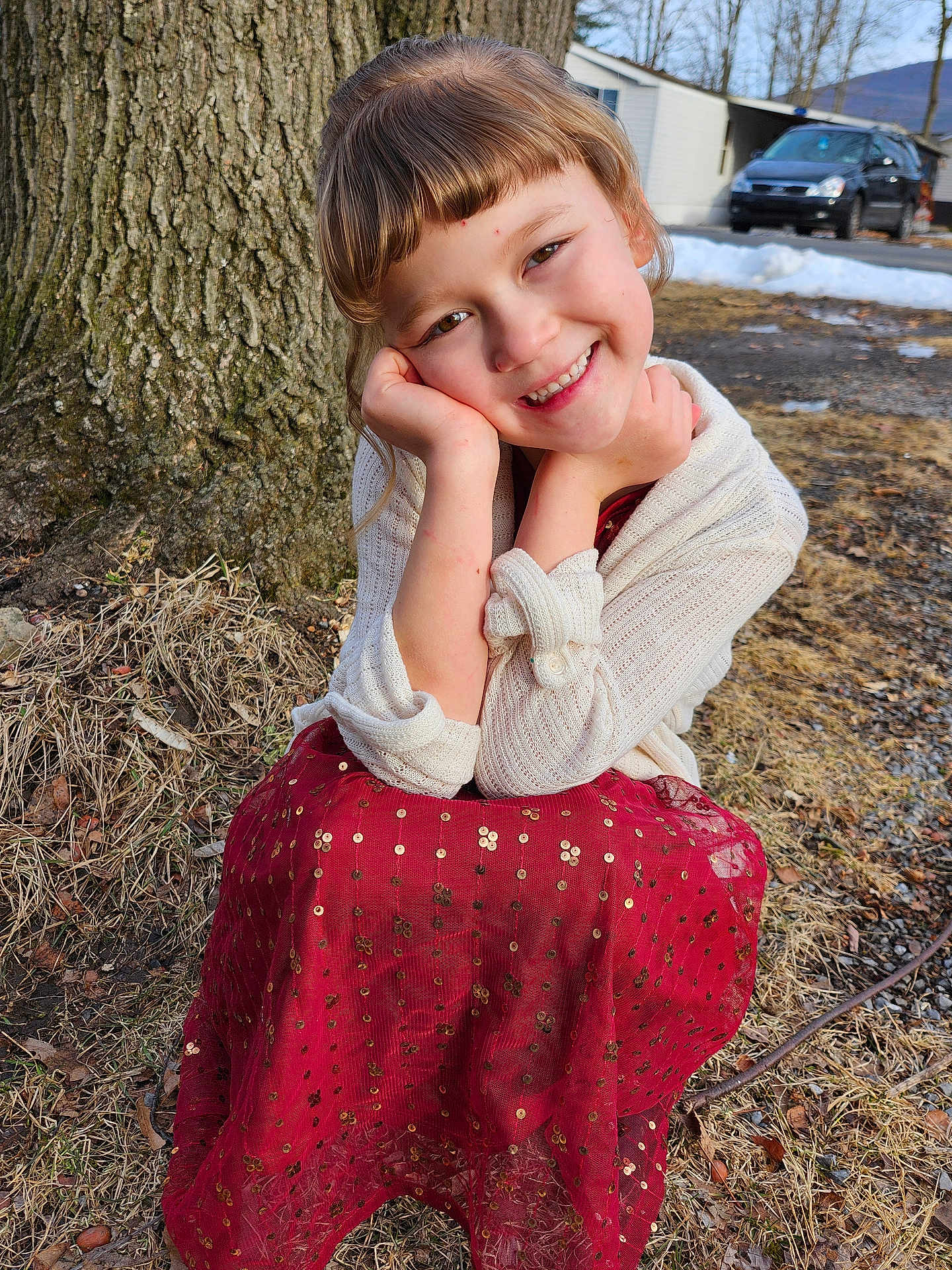 Yuvonne is registered to the contest to win money with this photo: child, smiling, red_dress, white_sweater, tree, outdoor, grass, snow, car, winter, happy, face, portrait, nature, cute, young, person, seasonal, ground, daylight