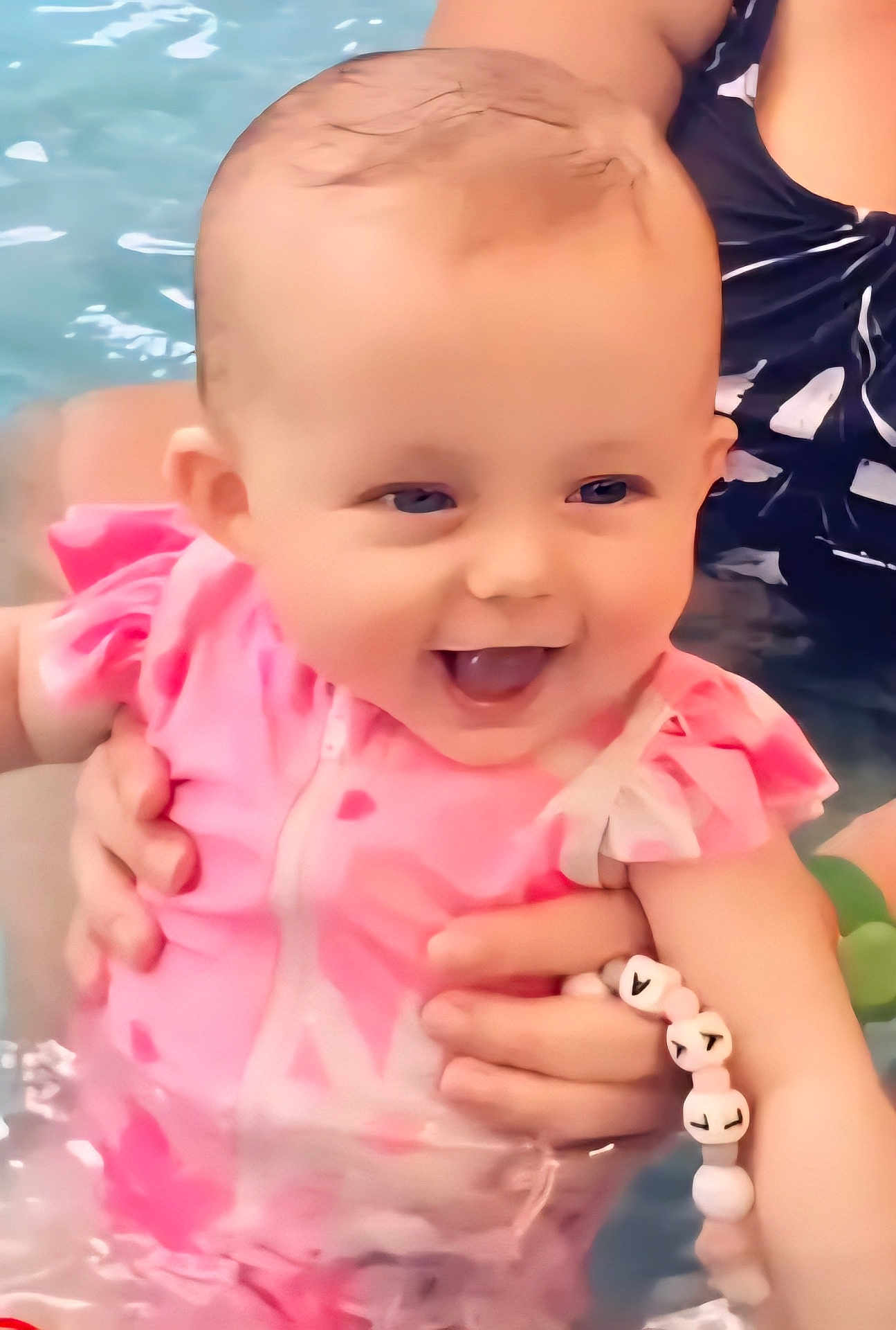 Lya a rejoint le concours — aidez-le/la à gagner de superbes lots ! baby, smiling, pink_swimsuit, water, pool, child, happy, holding_hands, bracelet, swimming, face, cute, summer, outdoor, person, playful, splash, fun, joy, infant