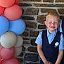 Enzo a rejoint le concours — aidez-le/la à gagner de superbes lots ! child, boy, smiling, balloons, stone_wall, vest, blue_shirt, happy, portrait, celebration, event, formal_wear, young, standing, colorful, pastel_colors, outdoor, person, cute, flower_boutonniere