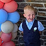 child, boy, smiling, balloons, vest, shirt, stone_wall, blue, red, pastel_colors, happy, portrait, party, celebration, flower_boutonniere, short_hair, indoors, cute, formal_wear, standing