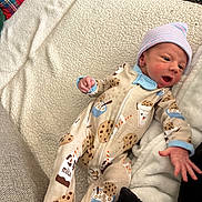 Ziah is registered to the contest to win money with this photo: newborn, baby, infant, onesie, hat, blanket, couch, pattern, milk, cookie, sleepwear, hand, face, person, soft, cozy, cute, lying_down, indoor, resting