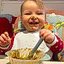 Elyo participe au concours pour gagner de l'argent avec cette photo : toddler, child, baby_food, high_chair, messy_face, spoon, bowl, smiling, happy, indoor, feeding, clothing, polka_dot, bib, table, hair, face, person, kitchen, seat