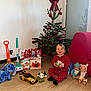 child, christmas_decorations, christmas_tree, dolls, festive, floor, happy, holiday, holiday_season, indoor, living_room, plush_toy, polka_dots, red_bow, red_pajamas, smiling, toddler, toy_car, toys, wooden_floor