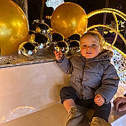 Elyo a rejoint le concours — aidez-le/la à gagner de superbes lots ! child, toddler, coat, shoes, bench, holiday_lights, decorations, baubles, gold, silver, reindeer, night, outdoor, festive, smile, winter, park, celebration, person, cute