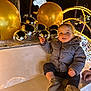 child, toddler, coat, shoes, bench, holiday_lights, decorations, baubles, gold, silver, reindeer, night, outdoor, festive, smile, winter, park, celebration, person, cute