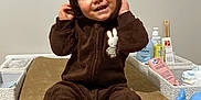 Elyo a rejoint le concours — aidez-le/la à gagner de superbes lots ! toddler, child, baby, onesie, brown_clothing, smiling, face, hood, ears, sitting, changing_pad, baby_care, bottle, diapers, table, indoor, cute, happy, person, infant