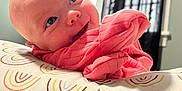 Clementine is registered to the contest to win money with this photo: baby, infant, smiling, face, blue_eyes, pink_clothing, cushion, patterned_fabric, window, curtains, indoor, natural_light, happy, resting, closeup, skin, head, cheeks, child, portrait