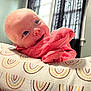 baby, infant, smiling, face, blue_eyes, pink_clothing, cushion, patterned_fabric, window, curtains, indoor, natural_light, happy, resting, closeup, skin, head, cheeks, child, portrait