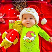 Joy participe au concours pour gagner de l'argent avec cette photo : baby, child, christmas, christmas_hat, cute, face, festive, green_outfit, grinch, holiday, holiday_theme, infant, lying_down, person, plush_toy, red_background, smiling, soft_toy, stuffed_animal, toddler