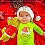 baby, child, infant, grinch, plush_toy, stuffed_animal, christmas_hat, holiday, festive, red_background, green_outfit, face, cute, smiling, lying_down, soft_toy, christmas, toddler, holiday_theme, person