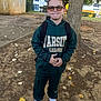 child, boy, outdoor, tree, backpack, sunglasses, hoodie, sweatpants, white_shoes, autumn, leaves, sidewalk, smile, standing, casual_clothing, young, playful, ground, person, nature