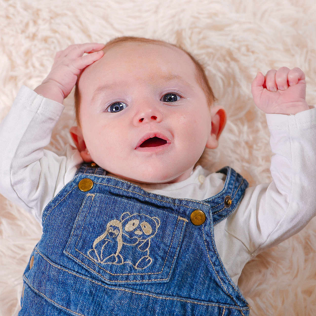 Milann participe au concours pour gagner de l'argent avec cette photo : adorable, baby, blue_eyes, casual_clothing, child, closeup, cute, denim_overalls, expression, face, fluffy_rug, hands, indoor, infant, lying_down, portrait, smiling, soft_texture, white_shirt, young