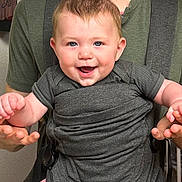 Waylon joined the competition — help win amazing prizes! baby, child, infant, baby_carrier, person, smiling, happy, blue_eyes, hair, clothing, hands, adult, indoor, closeup, face, skin, cute, joy, holding, green_shirt