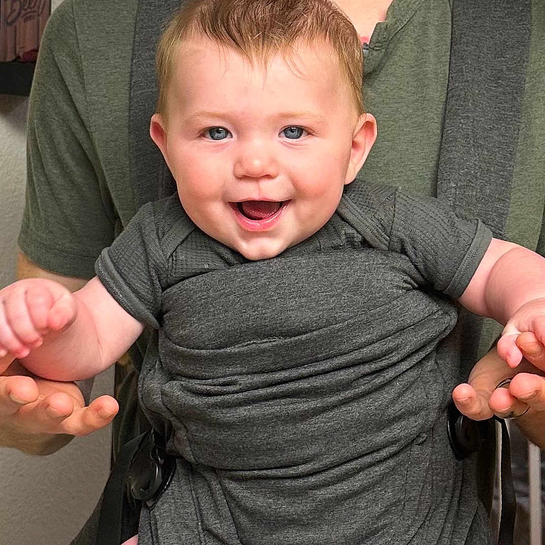 Waylon joined the competition — help win amazing prizes! adult, baby, baby_carrier, blue_eyes, child, closeup, clothing, cute, face, green_shirt, hair, hands, happy, holding, indoor, infant, joy, person, skin, smiling