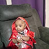 baby, child, costume, red_hood, couch, indoor, curtain, smiling, holding, seated, portrait, clothing, happy, cute, person, furniture, young_child, dark_hair, earring, playful