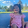 blue_sky, casual, child, clouds, girl, grass, hair, happy, necklace, outdoor, pink_dress, playful, shoes, smiling, static_electricity, sunny_day, text_overlay, toddler, trampoline, trees