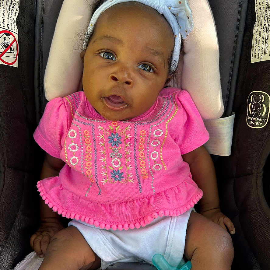 Jaleigha is registered to the contest to win money with this photo: baby, car_seat, child, closeup, colorful_clothing, comfort, cute, expression, headband, indoors, infant, looking_up, pacifier, person, pink_clothing, portrait, seat, seat_belt, white_headband, young_child