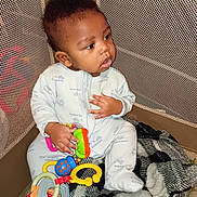 Miguel joined the competition — help win amazing prizes! baby, child, pajamas, toy, playpen, blanket, mesh, floor, indoor, cute, infant, clothing, sitting, colorful, hand, face, looking, young, person, comfort