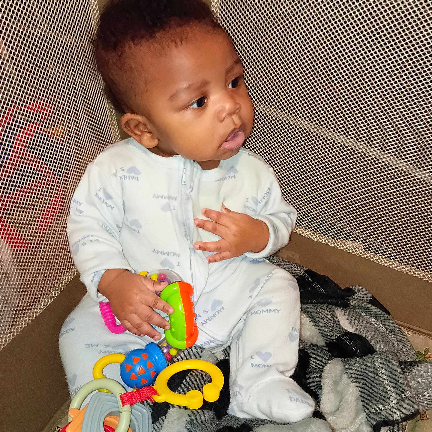 Miguel joined the competition — help win amazing prizes! baby, child, pajamas, toy, playpen, blanket, mesh, floor, indoor, cute, infant, clothing, sitting, colorful, hand, face, looking, young, person, comfort
