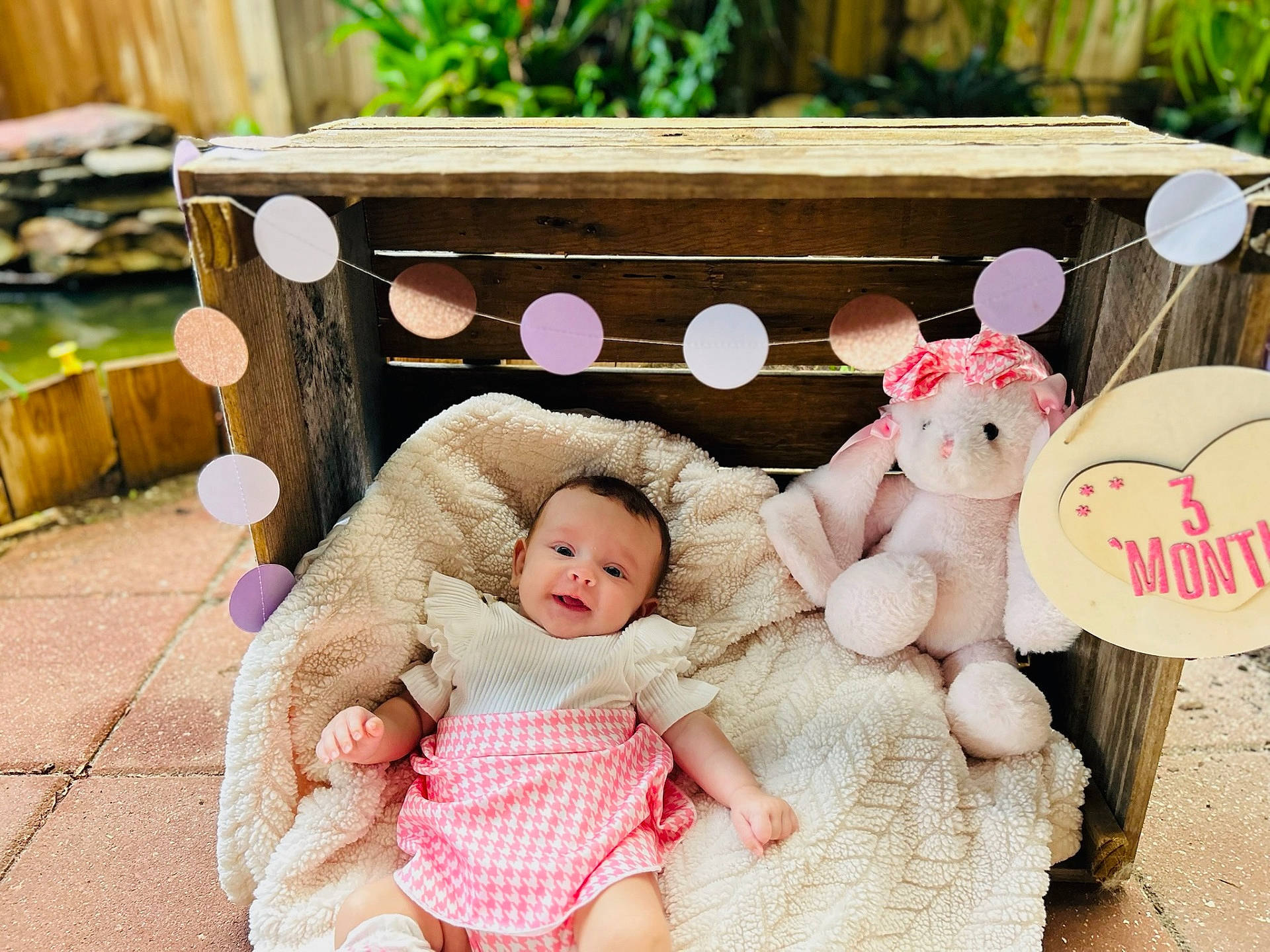 Alivia joined the competition — help win amazing prizes! baby, blanket, bunny, candid, cute, decoration, garden, garland, happy, heart_shape, infant, outdoor, pink_skirt, plush_toy, portrait, sign, smiling, soft_texture, white_top, wooden_crate