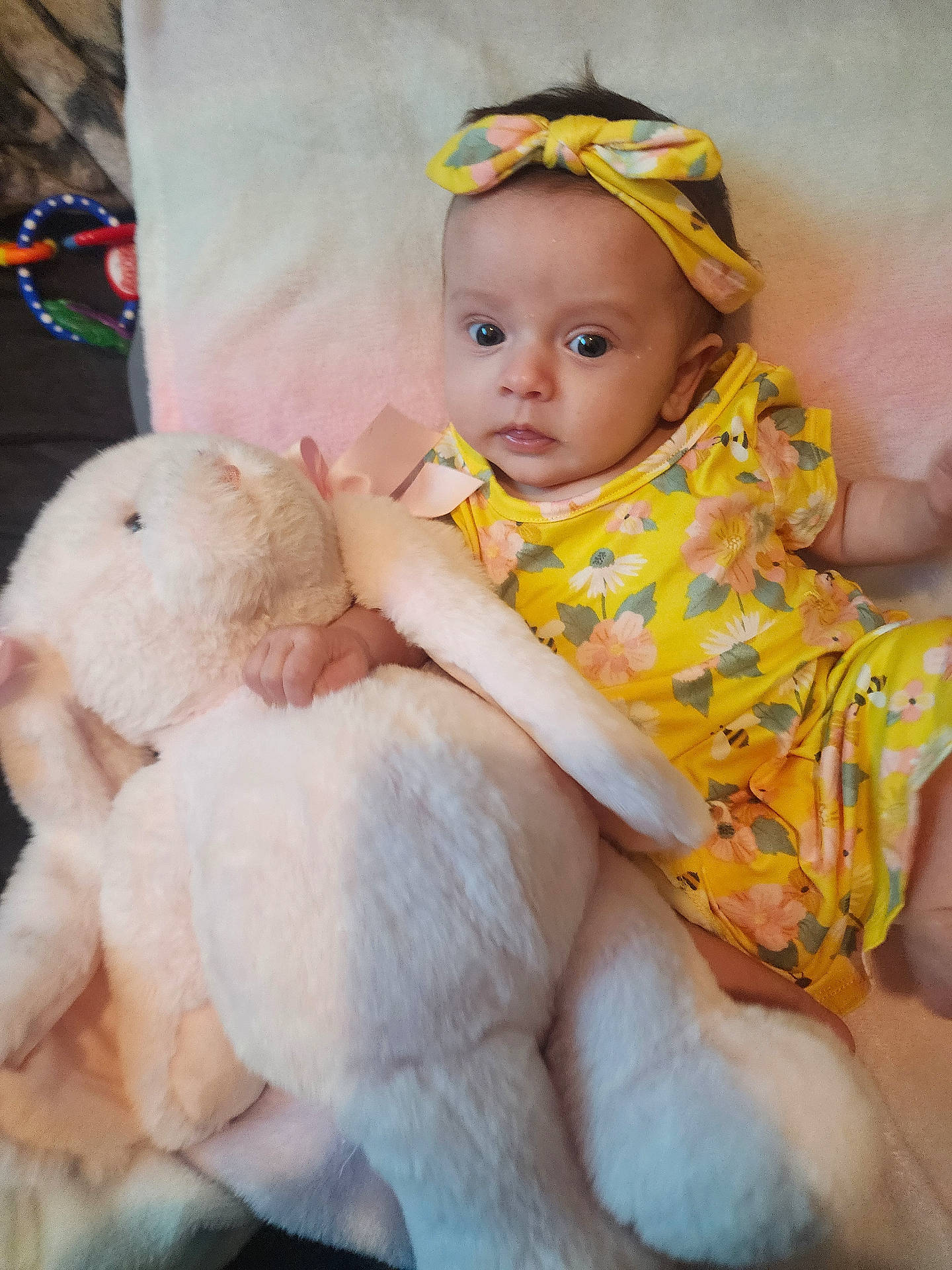baby, baby_girl, bed, blanket, child, colorful, comfort, cute, flower_pattern, headband, indoor, infant, plush_toy, portrait, resting, soft_toy, stuffed_animal, toy, yellow_clothing, young_child