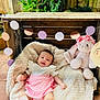 baby, blanket, candid, child, cute, decorations, face, garland, happy, head, infant, nature, outdoor, pink_clothing, plush_toy, portrait, sitting, smiling, soft_toy, wooden_crate