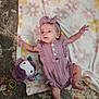 baby, infant, child, blanket, plush_toy, purple, mauve, headband, romper, carpet, floral_pattern, cute, lying_down, indoor, soft_toy, person, clothing, small_child, relaxed, baby_girl