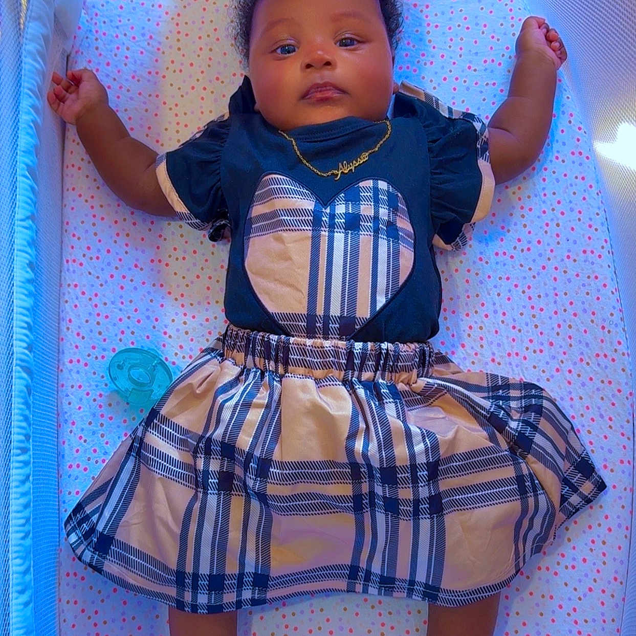 Alyssa is registered to the contest to win money with this photo: baby, infant, playpen, plaid_skirt, heart_socks, blue_lighting, pacifier, cute_clothing, child, lying_down, soft_toys, mesh_sides, patterned_blanket, adorable, portrait, indoors, calm_expression, small_hands, feet_up, necklace