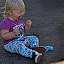 Harper is registered to the contest to win money with this photo: toddler, child, sitting, playful, purple_shirt, floral_pants, shoe, tongue_out, outdoor, asphalt, toy, blue_plush, happy, casual_clothing, person, young_child, cute, daylight, smiling, hair