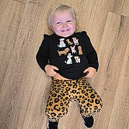 Harper joined the competition — help win amazing prizes! toddler, child, smiling, floor, wooden_floor, black_shirt, dog_illustration, leopard_print, pants, sneakers, happy, playful, indoor, person, clothing, cute, casual, laying_down, young_child, portrait