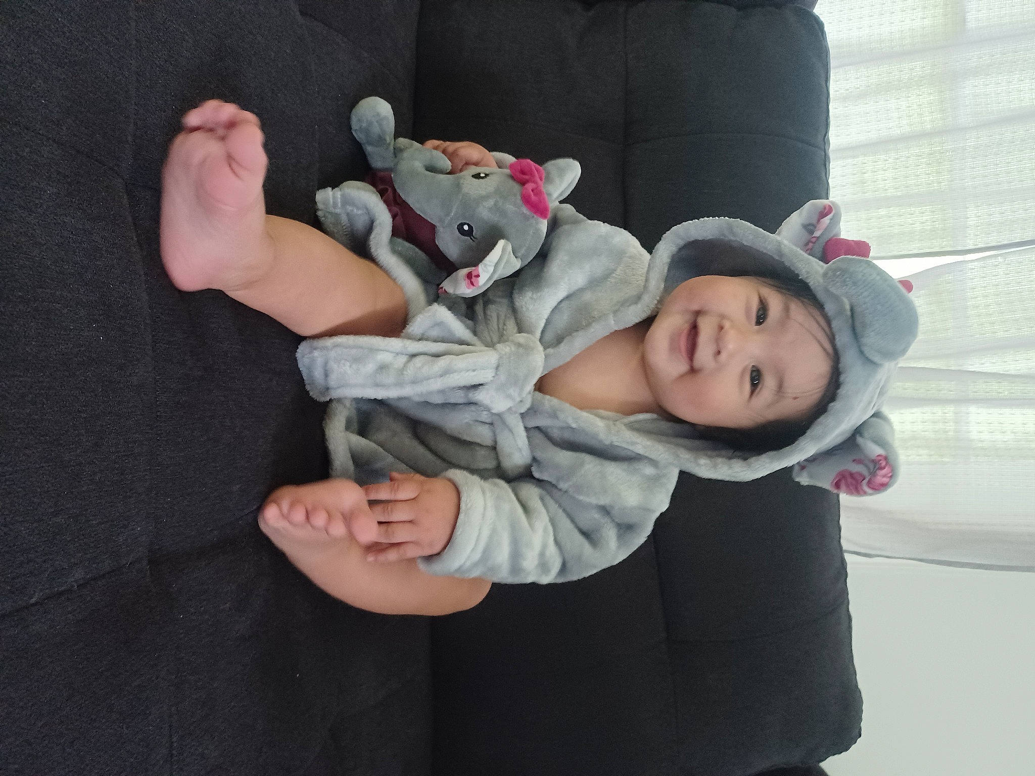 Elle is registered to the contest to win money with this photo: baby, baby_toddler_clothing, cap, child, comfort, foot, fun, gesture, grass, happy, hat, head, headwear, human_leg, joy, lap, person, sitting, smile, toddler