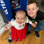 Edie joined the competition — help win amazing prizes! baby, child, smiling, red_dress, blue_sweater, indoor, wooden_floor, holding_hands, crouching, happy, people, footwear, radiator, clothing, boy, person, family, portrait, cute, toddler