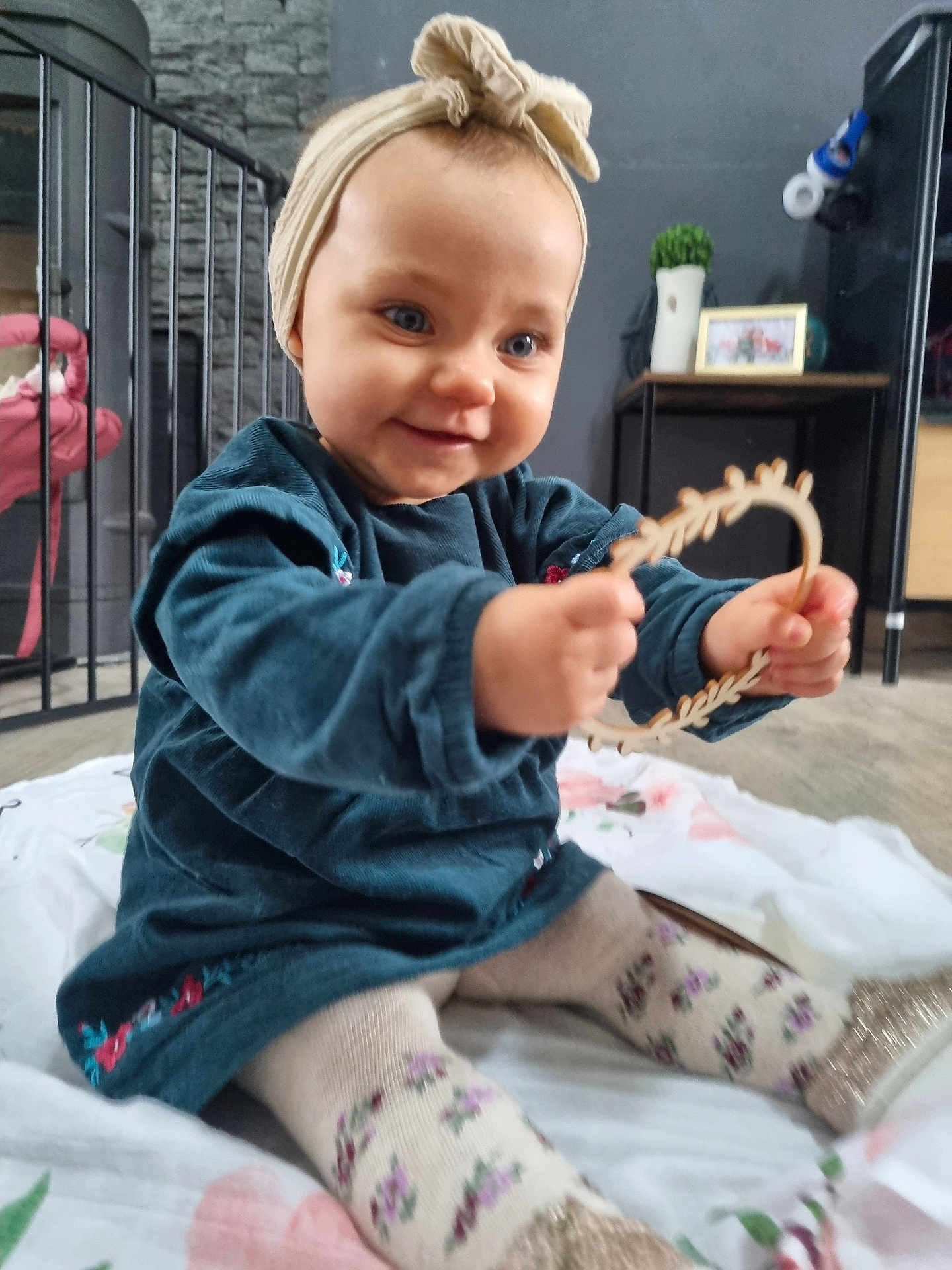 Mila participe au concours pour gagner de l'argent avec cette photo : baby, child, indoor, smiling, blue_dress, tights, floral_pattern, headband, wooden_toy, blanket, floor, furniture, table, decor, picture_frame, plant, curious, sitting, happy, cute