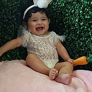 Aitana is registered to the contest to win money with this photo: baby, bunny_ears, carrot_toy, child, cute, expression, face, greenery, happy, infant, lace_outfit, plush_toy, pink_blanket, portrait, sitting, smiling, soft_texture, toy, white_clothing, young_child