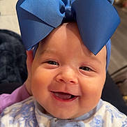 Millie is registered to the contest to win money with this photo: baby, smiling, blue_bow, headwear, onesie, floral_pattern, child, face, happy, cute, infant, portrait, indoor, closeup, expression, apparel, person, young_child, cheerful, adorable
