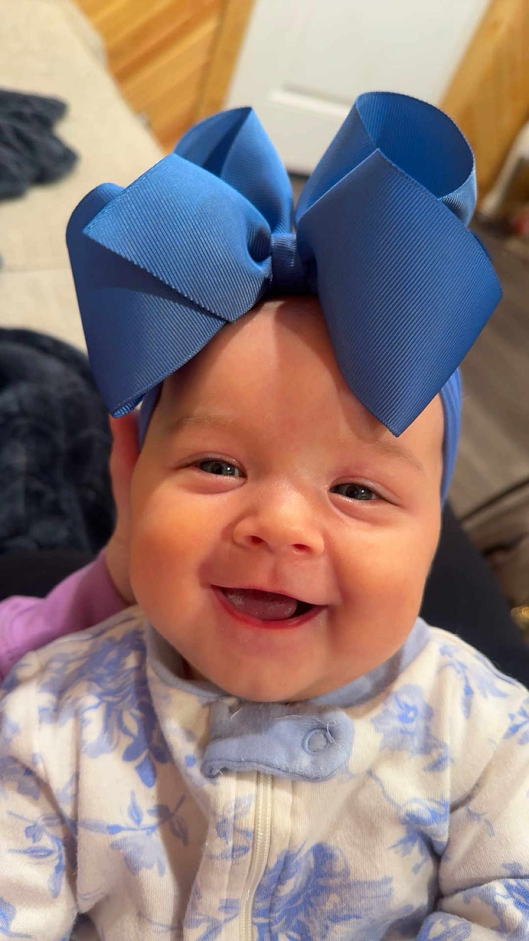 Millie is registered to the contest to win money with this photo: baby, smiling, blue_bow, headwear, onesie, floral_pattern, child, face, happy, cute, infant, portrait, indoor, closeup, expression, apparel, person, young_child, cheerful, adorable