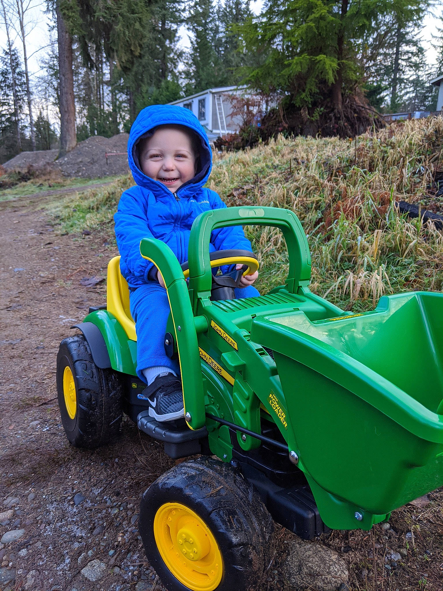 Boden is registered to the contest to win money with this photo: agricultural_machinery, child, fun, green, joy, person, plant, play, playground, public_space, riding_toy, soil, toddler, tractor, tree, vehicle