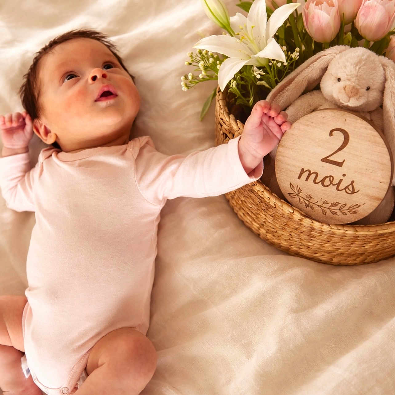 Israa participe au concours pour gagner de l'argent avec cette photo : baby, infant, onesie, blanket, basket, plush_bunny, flowers, wooden_sign, face, skin, cute, newborn, lying_down, soft_lighting, indoors, child, portrait, expression, toddler, celebration