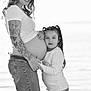 child, pregnant, woman, tattoo, embrace, outdoor, black_and_white, jeans, long_hair, smile, nature, water, family, love, casual_clothing, portrait, holding_hands, mother_and_daughter, pigtails, emotion