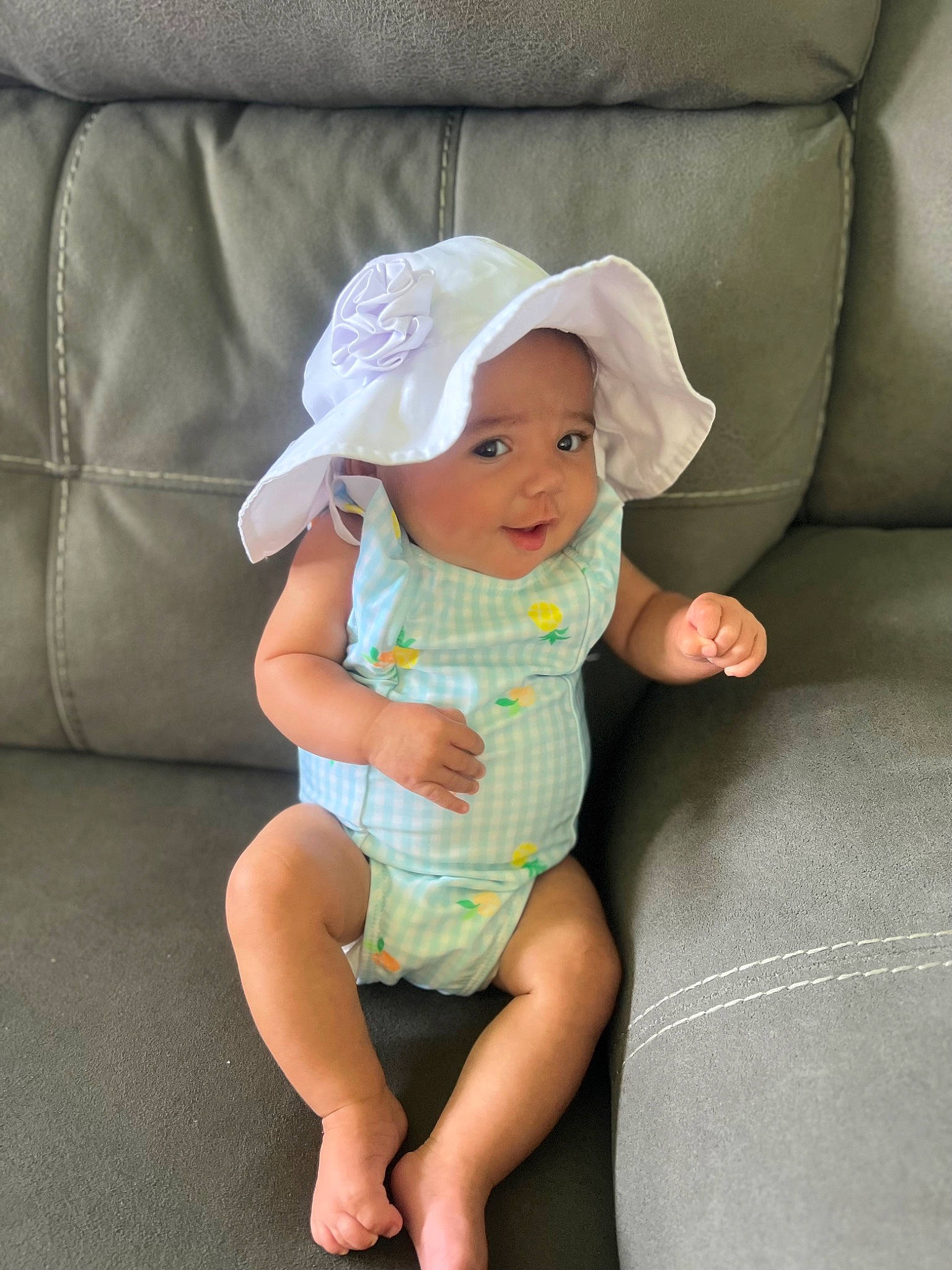 Clarissa is registered to the contest to win money with this photo: baby, baby_toddler_clothing, barefoot, cap, child, comfort, couch, foot, hat, headwear, human_body, human_leg, lap, leg, linens, pattern, person, sitting, sleeve, sun_hat
