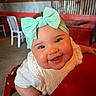 baby, child, smile, bow, headband, high_chair, restaurant, table, red, white_clothing, happy, face, cute, infant, curly_hair, interior, wooden_chair, person, closeup, portrait