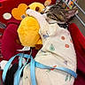 cat, kitten, plush_toy, shopping_cart, red_cart, blue_leash, clothing, snuggling, sleeping, cute, cozy, animal, pet, indoor, fabric, patterned_outfit, toy, comfort, close_up, resting
