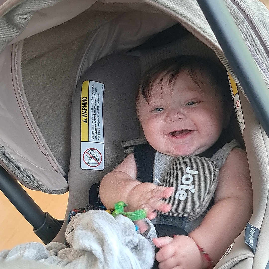 Ezequiel is registered to the contest to win money with this photo: baby, blanket, bright, canopy, car_seat, child, clothing, cushion, fabric, face, hand, happy, head_support, indoor, infant, person, protection, seatbelt, smiling, toy