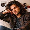 man, long_hair, plaid_shirt, couch, indoor, portrait, relaxed, cat, sleeping_cat, furry, cozy, inset_photo, young_adult, beard, hand_on_face, brown_hair, home, soft_light, website_text, casual